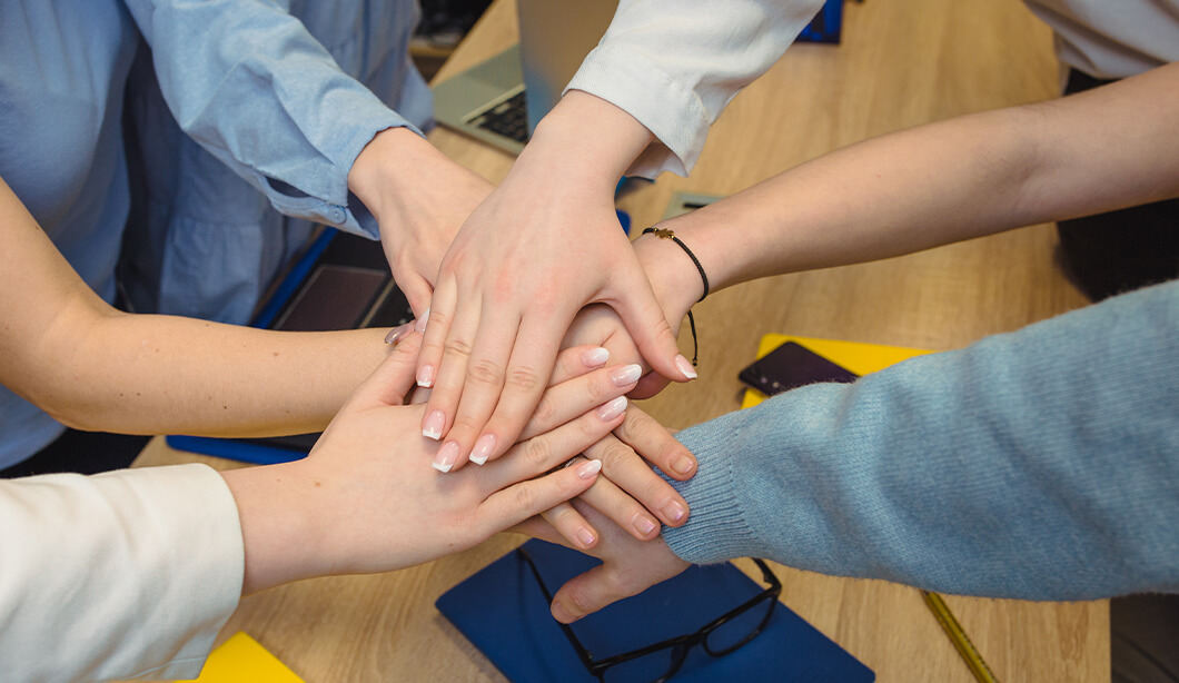 A photo of employees' hands stacked on top of each other in a gesture of cooperation